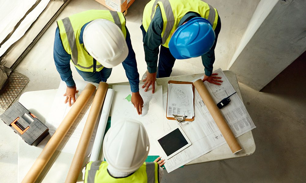 Blog - Top View of Contractors Discussing Over a Table with Documents and Plans