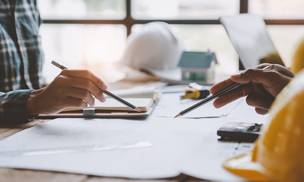 Blog - Two Contractors Sitting at a Table Pointing With Their Pencils at Documents in Front of them